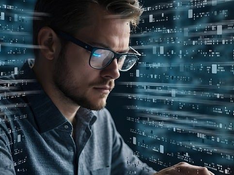 Mann mit Brille, fokussiert auf einen Computer, umgeben von binären Daten.