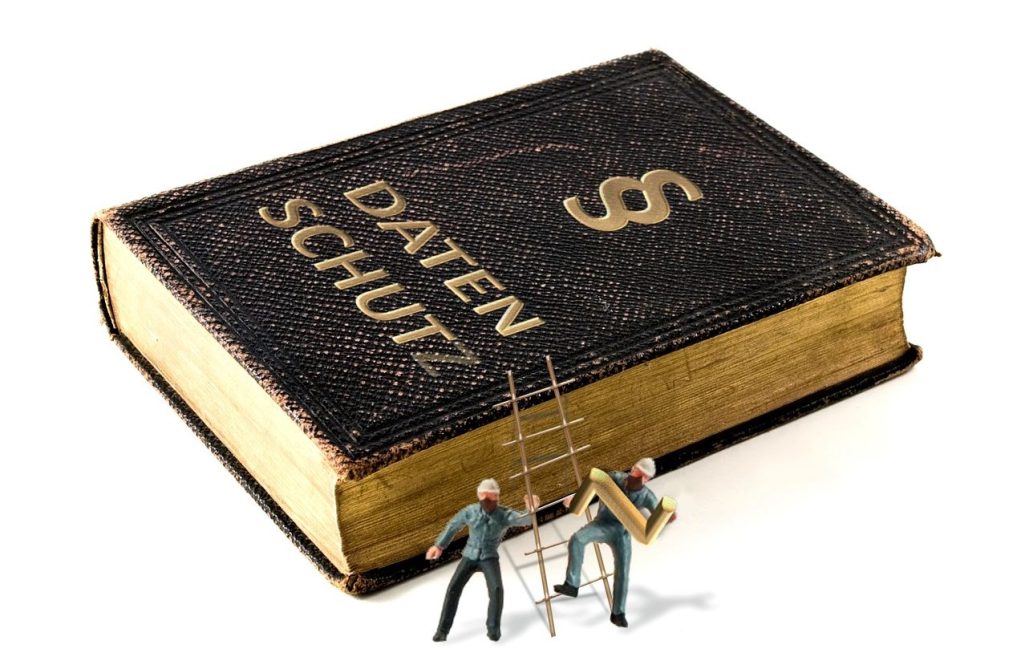 Zwei Miniaturfiguren arbeiten an einem großen Buch mit dem Titel "Datenschutz".