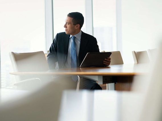 Mann mit Tablet sitzt nachdenklich an einem Konferenztisch in einem modernen Büro.